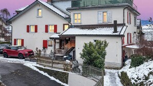 A two-story house with a balcony, a car parked in front, and a snow-covered path. - Elegant Lake Zurich House with Stunning Views and Private Terrace (Stäfa)