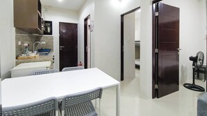 A modern kitchen with a white countertop, a sink, and a stove. There is a dining table with chairs and a dark wooden door. - Manzil Anilao Unit 1 - Ground Floor 1st Room (Mabini)