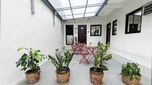 A corridor with a glass ceiling, potted plants, a red folding table, and a door with a sign. - Manzil Anilao Unit 1 - Ground Floor 1st Room (Mabini)