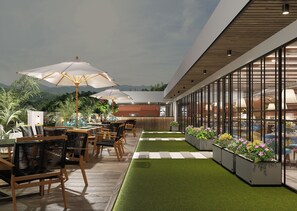 Een buitenzitgedeelte met tafels, stoelen en parasols, omgeven door plantenbakken en met uitzicht op de bergen.