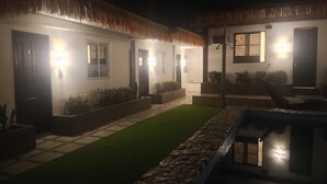 Vista nocturna de un edificio con techo de paja, piscina e interiores bien iluminados.