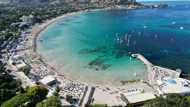 An aerial view of a coastal town with a beach, boats, and a mountainous backdrop. - Cloe House - Mondello (Palermo)
