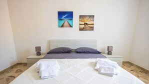 A neatly made bed with pillows and towels, two wall-mounted speakers, and two framed pictures depicting a pier and sunset. - Cloe House - Mondello (Palermo)