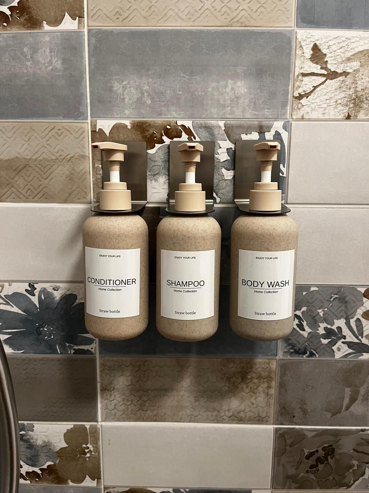 Trois flacons de produits de toilette, présentés comme une collection, sont posés sur un mur carrelé.
