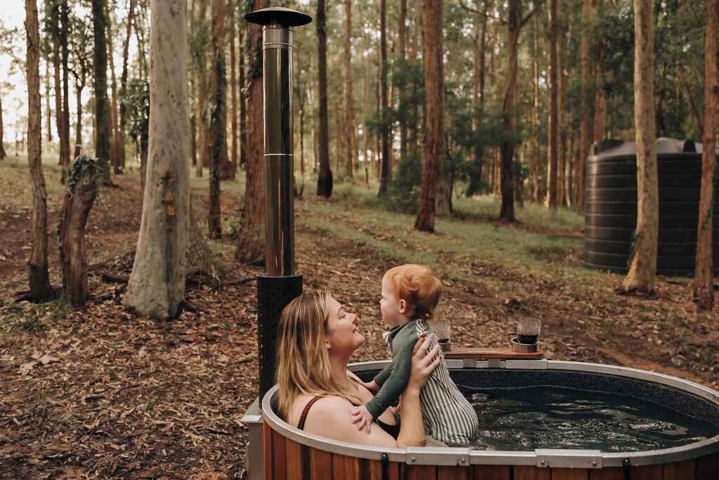 A hot tub in a forested area with a metal heater and a wooden deck.