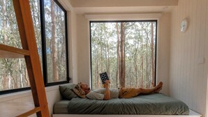 Un dormitorio con asiento empotrado junto a la ventana, una escalera y vistas a un bosque.