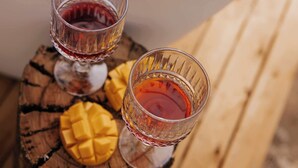 Twee glazen rode drank op een houten oppervlak met een mango.