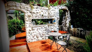 Un área de estar al aire libre de piedra con una barra integrada, cubierta de madera y una pequeña mesa con sillas.