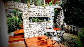 A stone-built outdoor seating area with a built-in bar, wooden deck, and a small table with chairs. - Room-charming Guest Room in Idyllic Ebbs (Ebbs)
