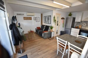 Un espacio habitable compacto con kitchenette, un sofá, una mesa de comedor y un perchero.