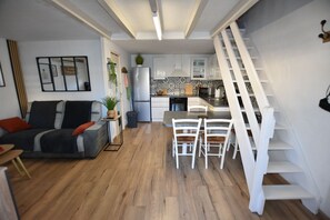 A modern living room with a sofa, a dining table with chairs, a kitchen area, and a white staircase.