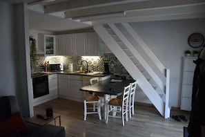 A compact kitchen with white cabinets, a dining table with chairs, a microwave, and a sink.