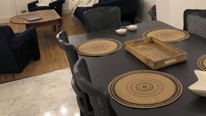 Een moderne woonkamer met een donkerbank, een eettafel met placemats en een plafondventilator.
