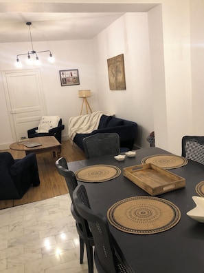 A modern living room with a dark-colored sofa, a dining table with placemats, and a ceiling fan. - House with garden, 20 minutes walk from the town centre (Yzeure)