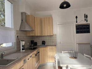 A kitchen with wooden cabinets, a white countertop, a stove, and a dining table with chairs. - House with garden, 20 minutes walk from the town centre (Yzeure)