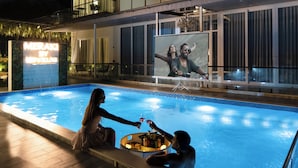 Una piscina con zona de bar, un cartel grande iluminado y vistas de la piscina desde el interior de un edificio.