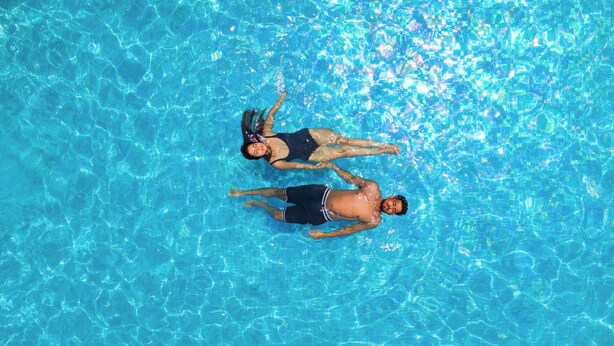 Dos personas flotando en una piscina azul cristalina.