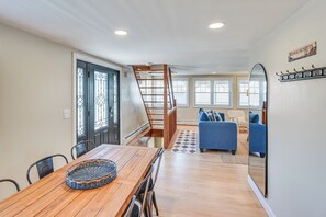 A dining area with a wooden table and chairs, a staircase, a living room with a sofa and a mirror, and a sign indicating the location.