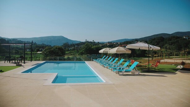A swimming pool with lounge chairs and umbrellas, surrounded by a landscaped area with a view of distant hills. - Sandoco House - Pitch&putt Golf - Pool & Nature (Ponte de Lima)