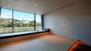 Una habitación con suelo de tatami, un ventanal con vistas a edificios y vegetación, y un banco empotrado.