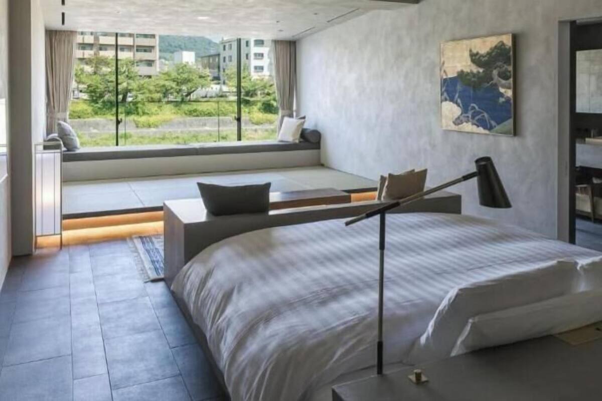 A modern bedroom with a bed, bedside tables, a window seat, and a painting.