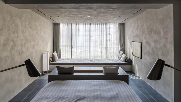 Un dormitorio moderno con una cama grande, un banco y una ventana con cortinas translúcidas.