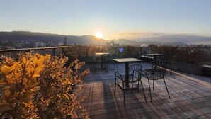 Terraza en la azotea con mesas y sillas, con vistas a un paisaje urbano y montañas.