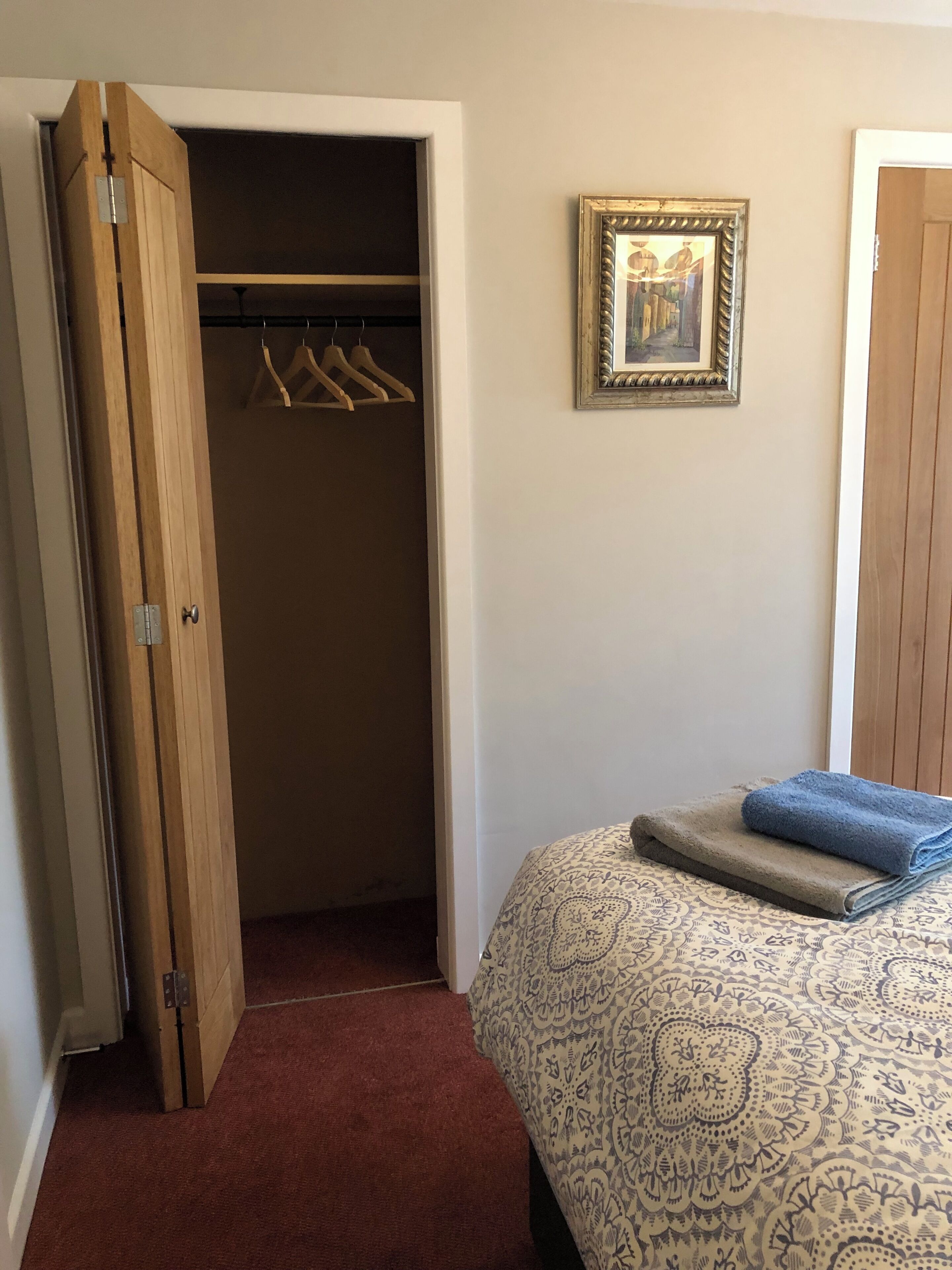 Un dormitorio con una cama, un armario con perchas y un cuadro enmarcado en la pared.