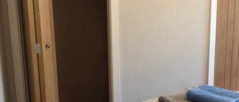 Un dormitorio con una cama, un armario con perchas y un cuadro enmarcado en la pared.