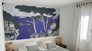 Une chambre à coucher avec un grand lit, deux tables de chevet avec des lampes, une fresque murale et une fenêtre avec des rideaux.