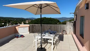 Une terrasse sur le toit, avec une table et des chaises, un grand parasol et une vue sur le paysage.