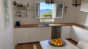 Une cuisine avec des meubles blancs, un plan de travail en bois, un évier, un lave-vaisselle et une table à manger agrémentée d’un panier de fruits.