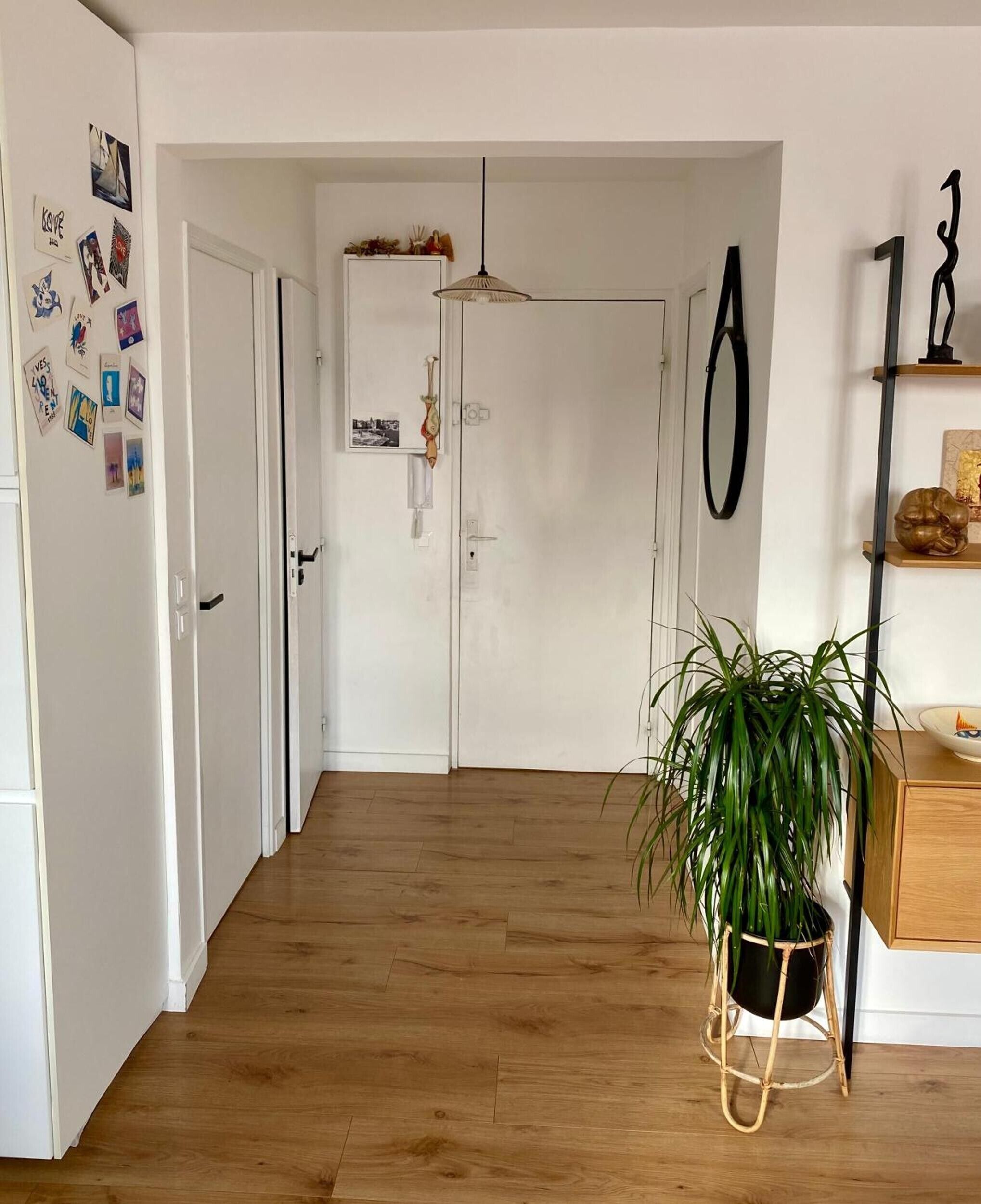 A hallway with wooden flooring, white walls, a potted plant, and a door with a hanging ornament.