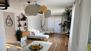 Un salon moderne avec un canapé blanc, une table à manger ornée de fruits et un coin cuisine doté d’un plancher en bois.