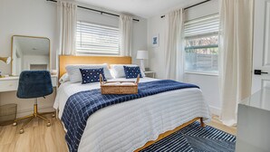 Et soveværelse med seng, skrivebord, stol, ventilator i loftet og vinduer med gardiner.