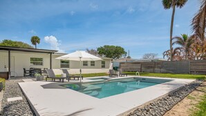En swimmingpool med liggestole, en overdækket terrasse og et hus i baggrunden.