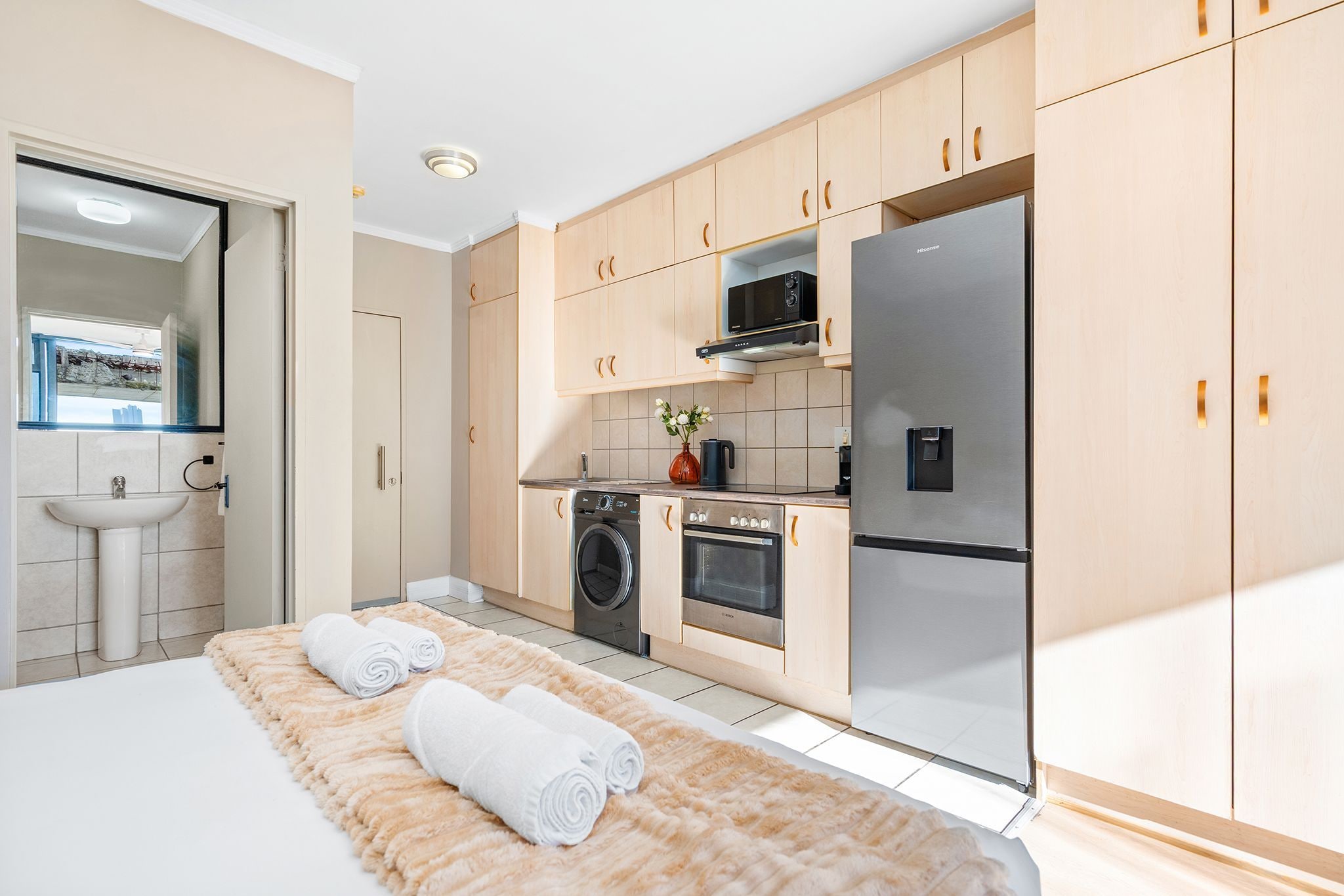 A modern kitchen with wooden cabinets, a stainless steel refrigerator, a microwave, and a washing machine.