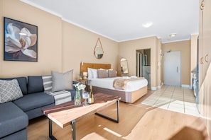 A modern hotel room with a sofa, a bed, a wooden coffee table, and a large flower painting on the wall. - Four Seasons Urban Escape (Cape Town)