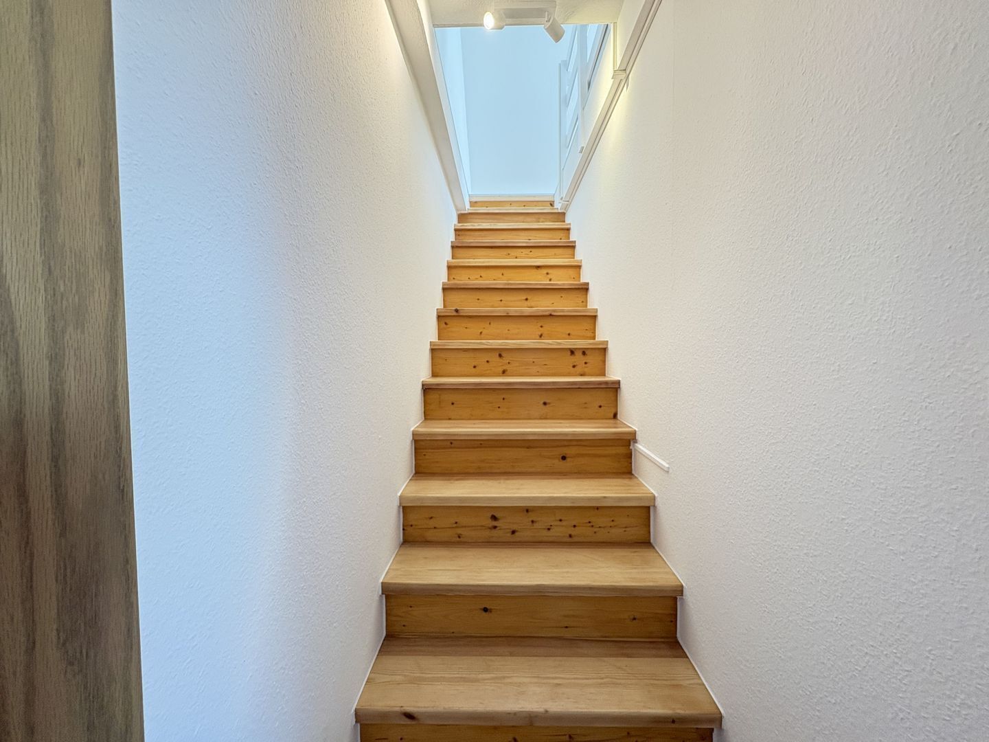 A wooden staircase with white walls and a skylight at the top.