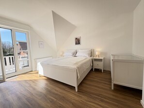 A bedroom with a bed, bedside tables, a nightstand, a radiator, and a view through a glass door.