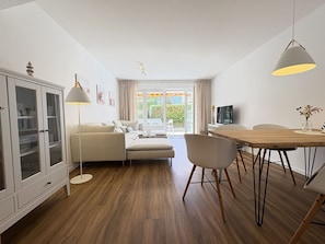 Un salon moderne comprenant un canapé, une table à manger, des chaises, un meuble et un téléviseur.