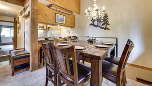 A dining area with a wooden table set for four, surrounded by chairs, a chandelier, and a wall-mounted decoration. - 1 Mi to Shaver Lake! Family & Couples Condo (Shaver Lake)