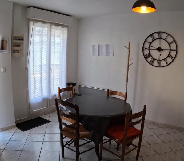 Comedor con una mesa redonda, cuatro sillas, un reloj de pared y una ventana con cortinas.