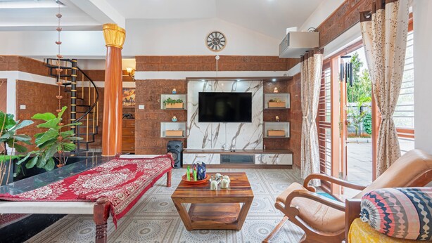 Un amplio salón con televisor, muebles de madera, alfombra roja con estampado y una escalera.