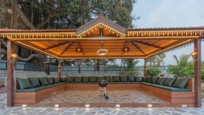 Un espacio de estar al aire libre techado, con una parrilla, piso de baldosas de piedra y una pérgola de madera con luces.