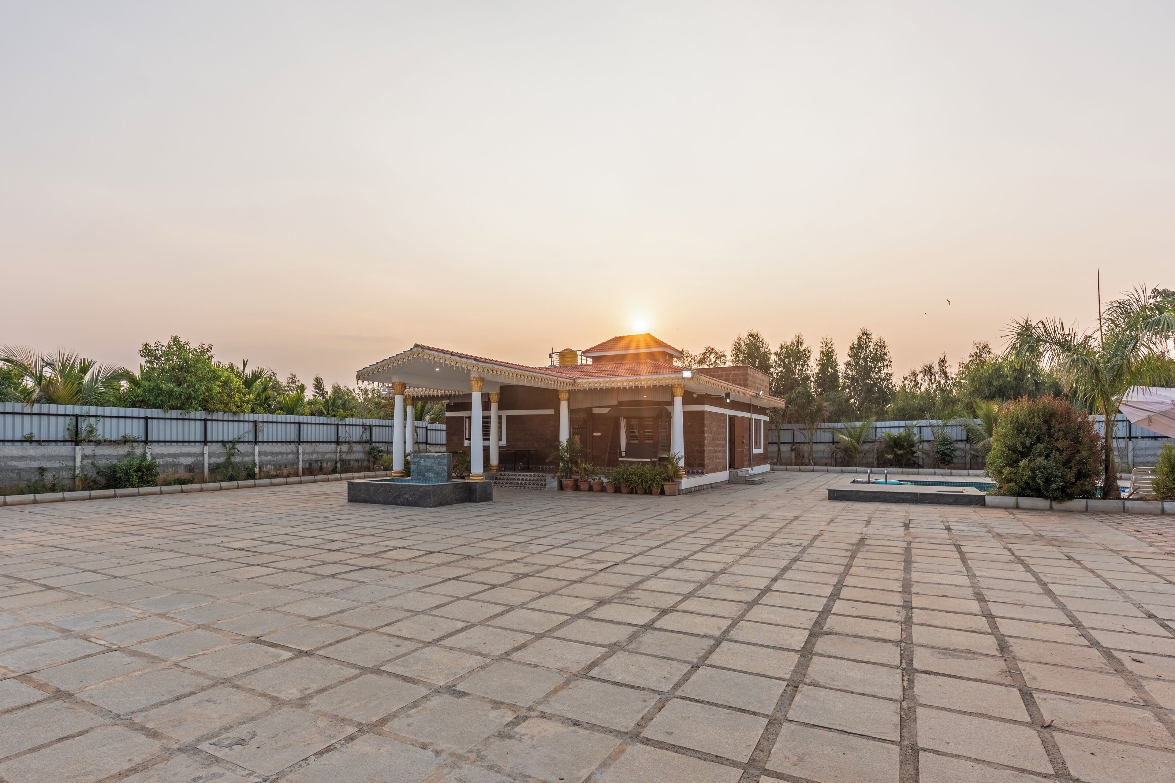 A courtyard with a pavilion, a tiled floor, and a fence.