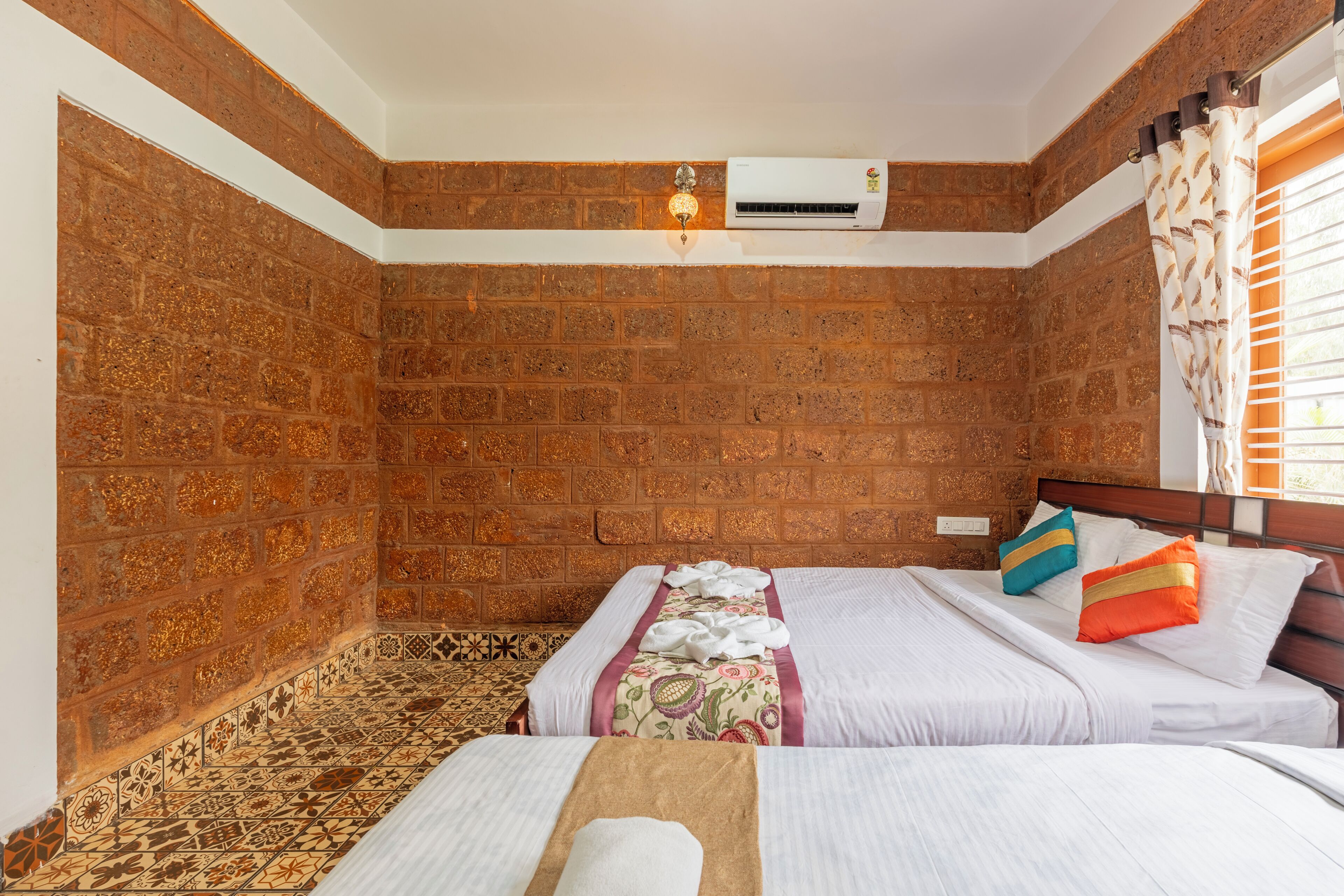 Une chambre avec deux lits, un mur en briques, un climatiseur et un revêtement de sol à motifs.