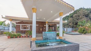 Un espacio exterior techado con una fuente de agua, plantas en macetas y un edificio con entrada de azulejos.