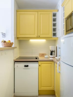 Eine kompakte Küche mit gelben Schränken, einem weißen Geschirrspüler und einem weißen Kühlschrank.