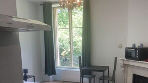 Una cocina compacta con microondas, una pequeña mesa de comedor y un ventanal con cortinas.